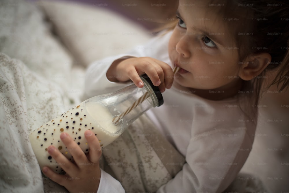 Milk for strong bones. Little girl drinking milk in the bed. Close up.