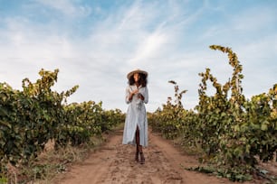 Young woman in a straw hat walking in a path in the middle of a vineyard with a bunch of grapes in hands