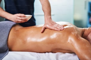 Primer plano de joven caballero desnudo recibiendo masaje en la espalda mientras está acostado en la mesa de masaje en el salón del spa