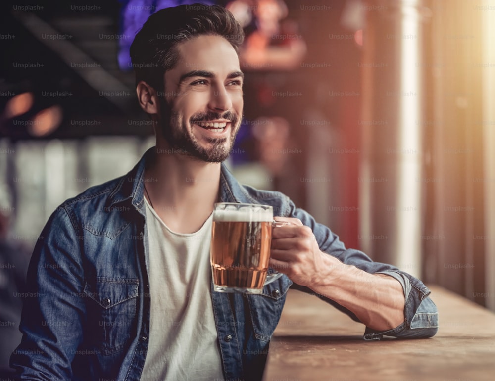 Jovem bonito está bebendo cerveja em bar e sorrindo