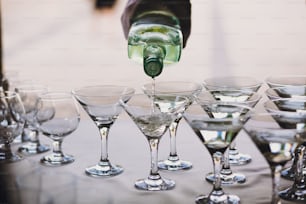 Kellner gießt Martini in Kristallgläser auf Tischparty bei der Hochzeitsfeier. Martini-Reihengetränke an der Alkoholbar. Weihnachts- und Neujahrsfest. Feiern und Partykonzept.