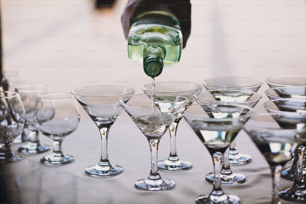 Waiter pouring martini in crystal glasses on table party at wedding reception. Martini row drinks at alcohol bar. Christmas and New Year feast. Celebrations and party concept.