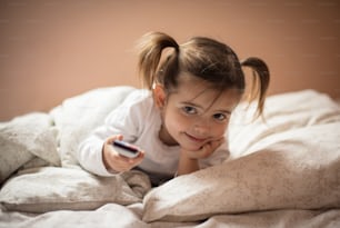 It's okay for me to watch TV. Little girl holding remote. Close up.