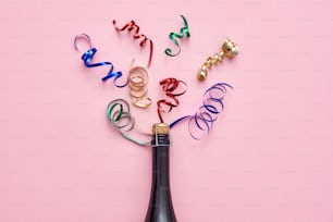 Party up. A bottle of champagne with shiny ribbons on pink background. Top view