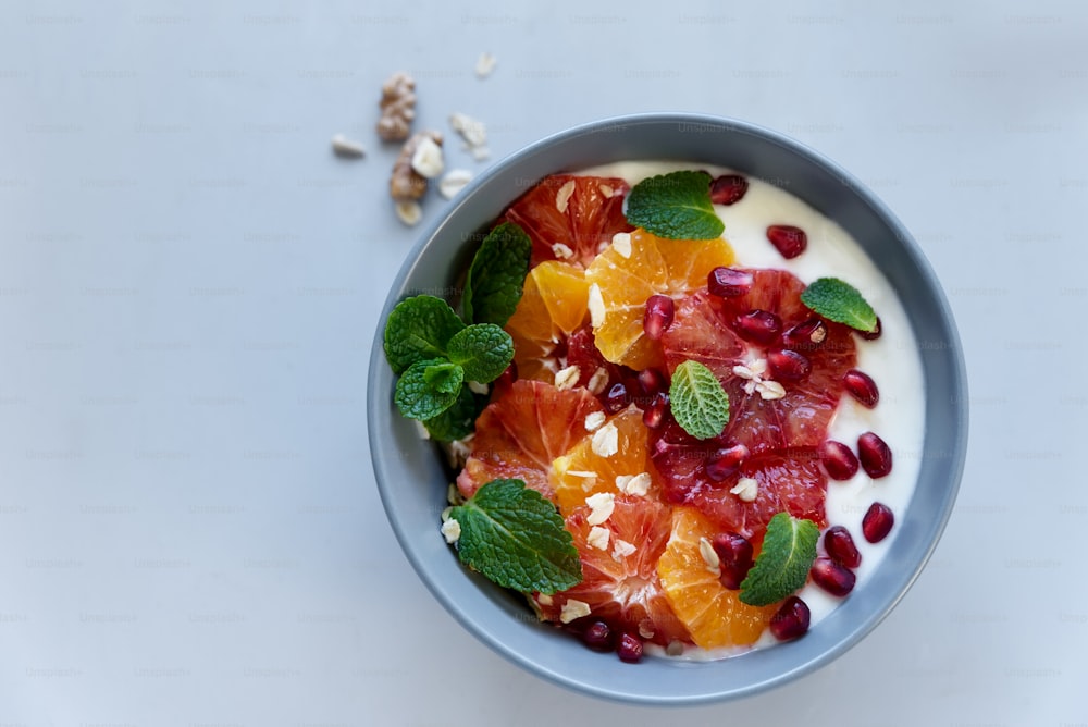 Bowl of homemade granola with yogurt, citrus and pomegranate seeds on gray wooden background. Selective focus. Healthy eating or vegetarian food concept