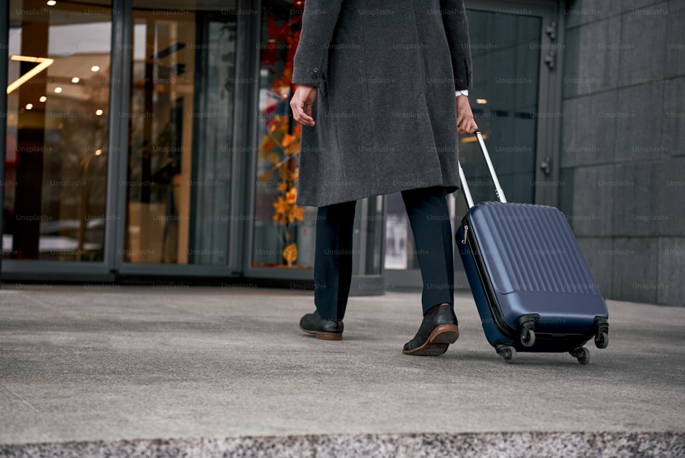 Primer plano de un hombre que lleva una maleta en la terminal del aeropuerto y se apresura a registrarse en un viaje de vacaciones o de negocios.