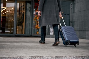 空港ターミナルでスーツケースを運び、休暇や出張でチェックインを急ぐ男性の接写。