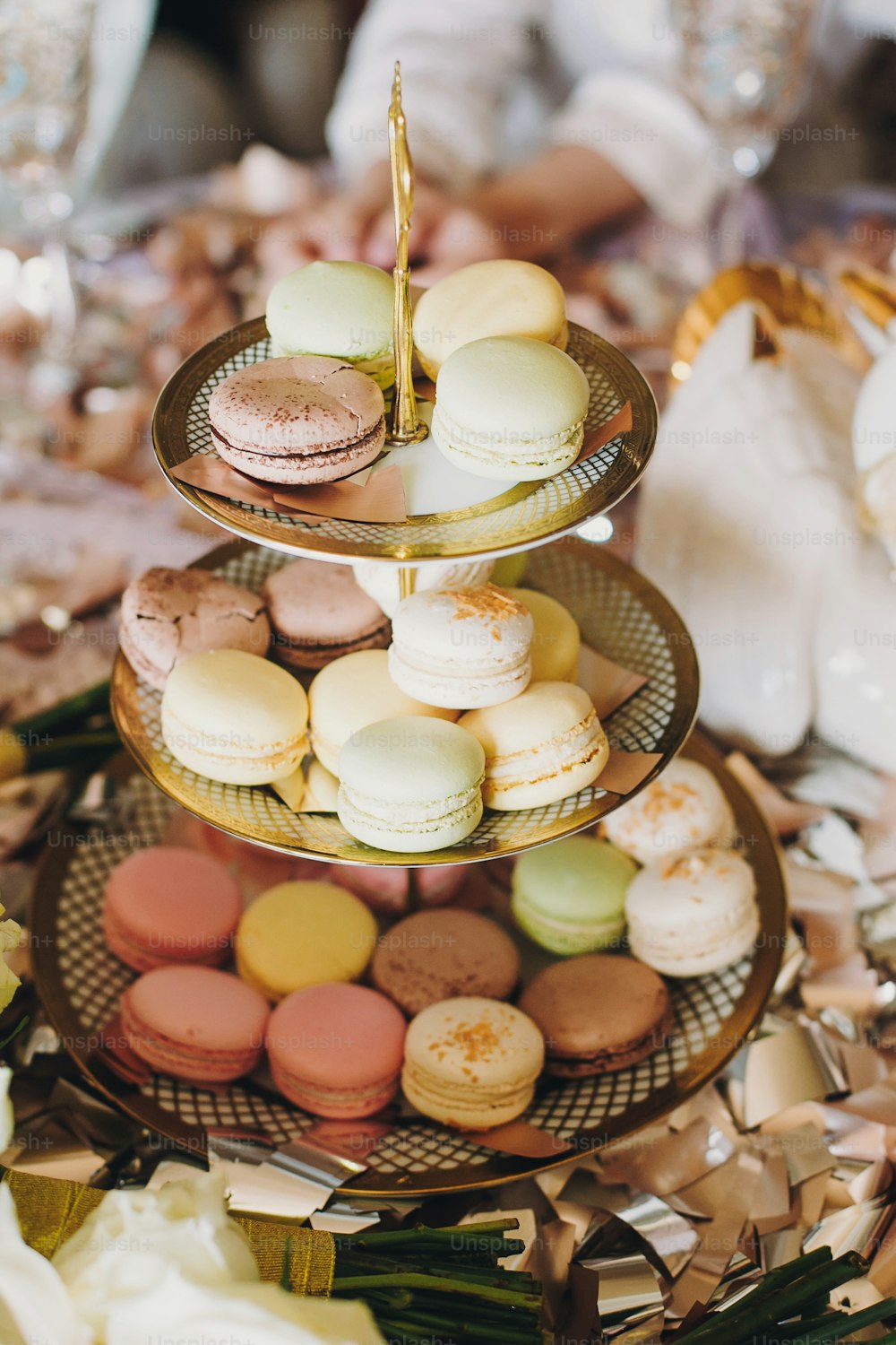 Delicious colorful macarons on beautiful vintage stand with gold ornaments on table with gold and silver confetti. Luxury catering. Bridal hen or baby shower. French dessert macaroons