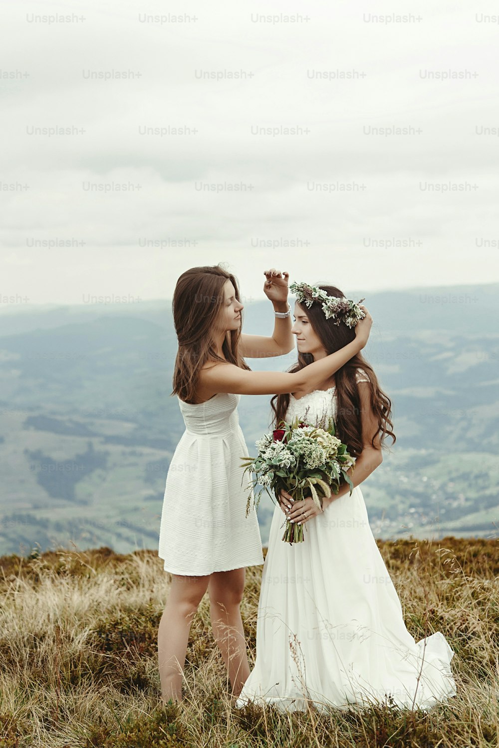 stylish bridesmaid helping gorgeous bride preparing, boho wedding, luxury ceremony at mountains