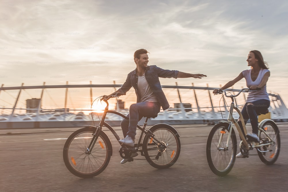 아름다운 낭만적 인 커플은 일몰에 자전거와 함께 도시에서 휴식을 취하고 있습니다. 서로의 회사를 즐깁니다.