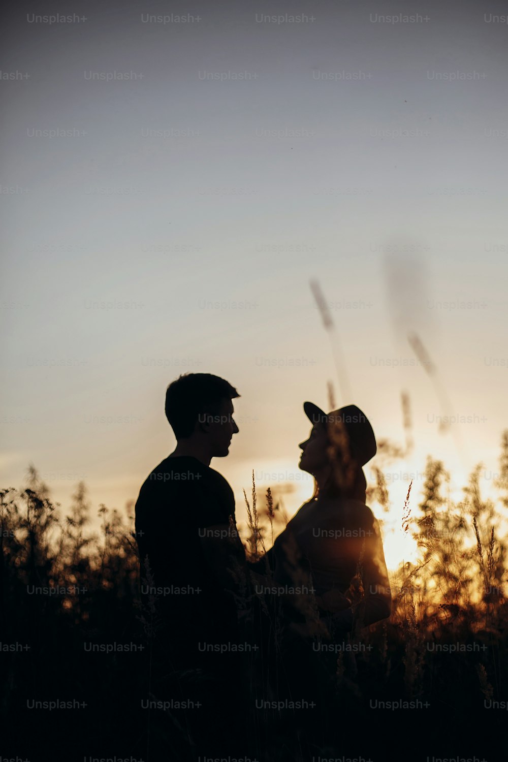 Stylish pregnant couple silhouettes in sunny light in autumn park among grass. Happy young parents, mom and dad, hugging baby bump, enjoying beautiful moment at sunset. Parenthood concept