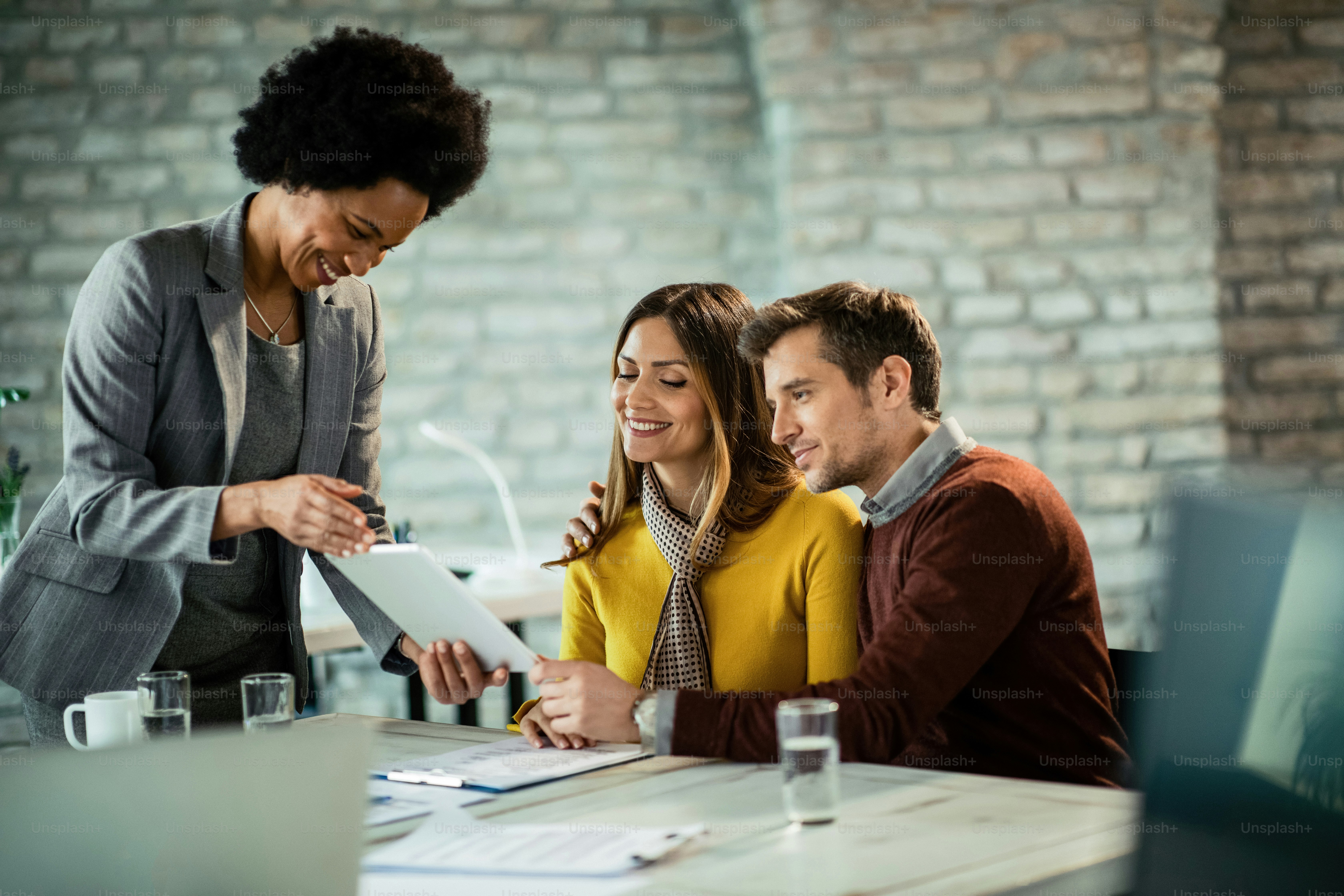 Happy couple and African American insurance agent looking at savings plan on touchpad in the office.