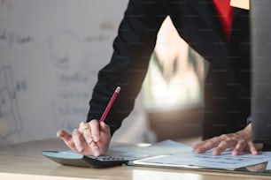 Plan d’une femme d’affaires utilisant une calculatrice pour calculer les chiffres du rapport de documents financiers sur son bureau dans un bureau.