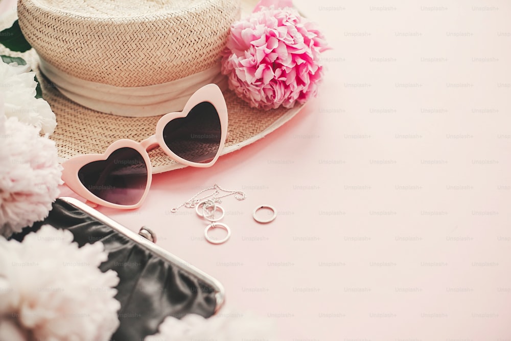 Óculos de sol elegantes, joias, chapéu de palha, bolsa rosa e buquê de peônias brancas em papel rosa com espaço para texto. Olá verão.  Dia Internacional da Mulher.