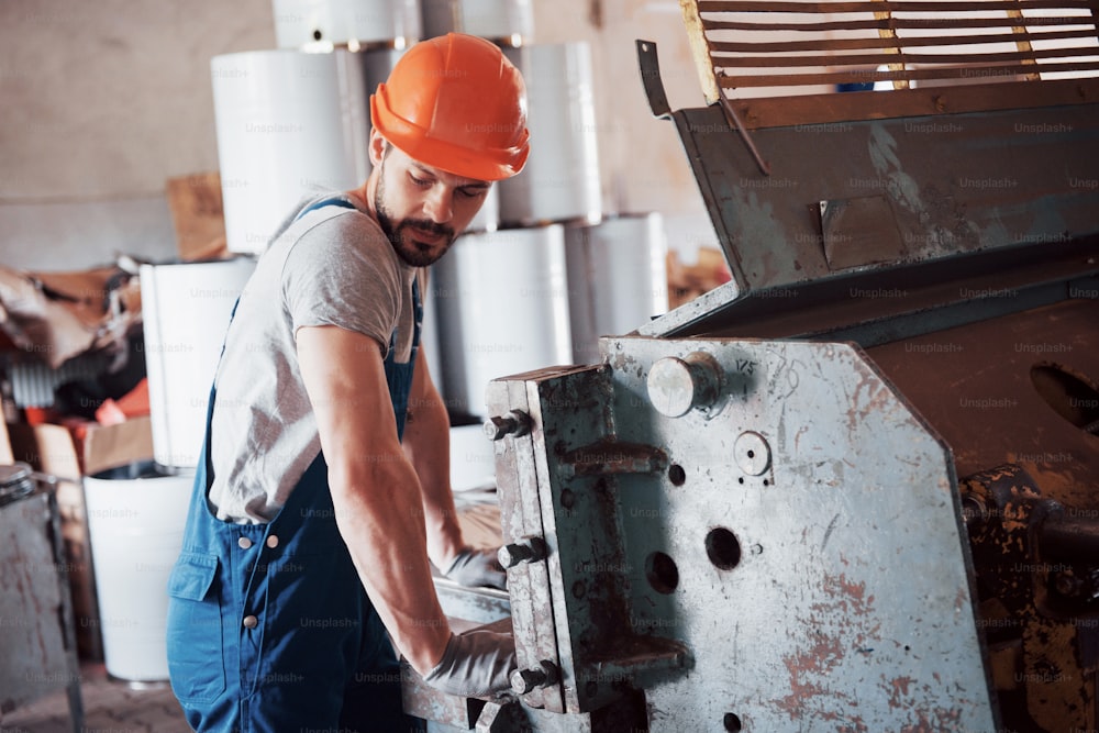 Portrait of a young worker in a hard hat at a large waste recycling factory. The engineer monitors the work of machines and other equipment.