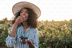 Mulher jovem feliz em um chapéu de palha comendo uvas em um vinhedo