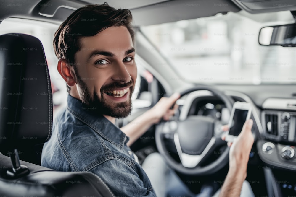 Young man is choosing a new vehicle at car dealership, smiling and looking at the camera.