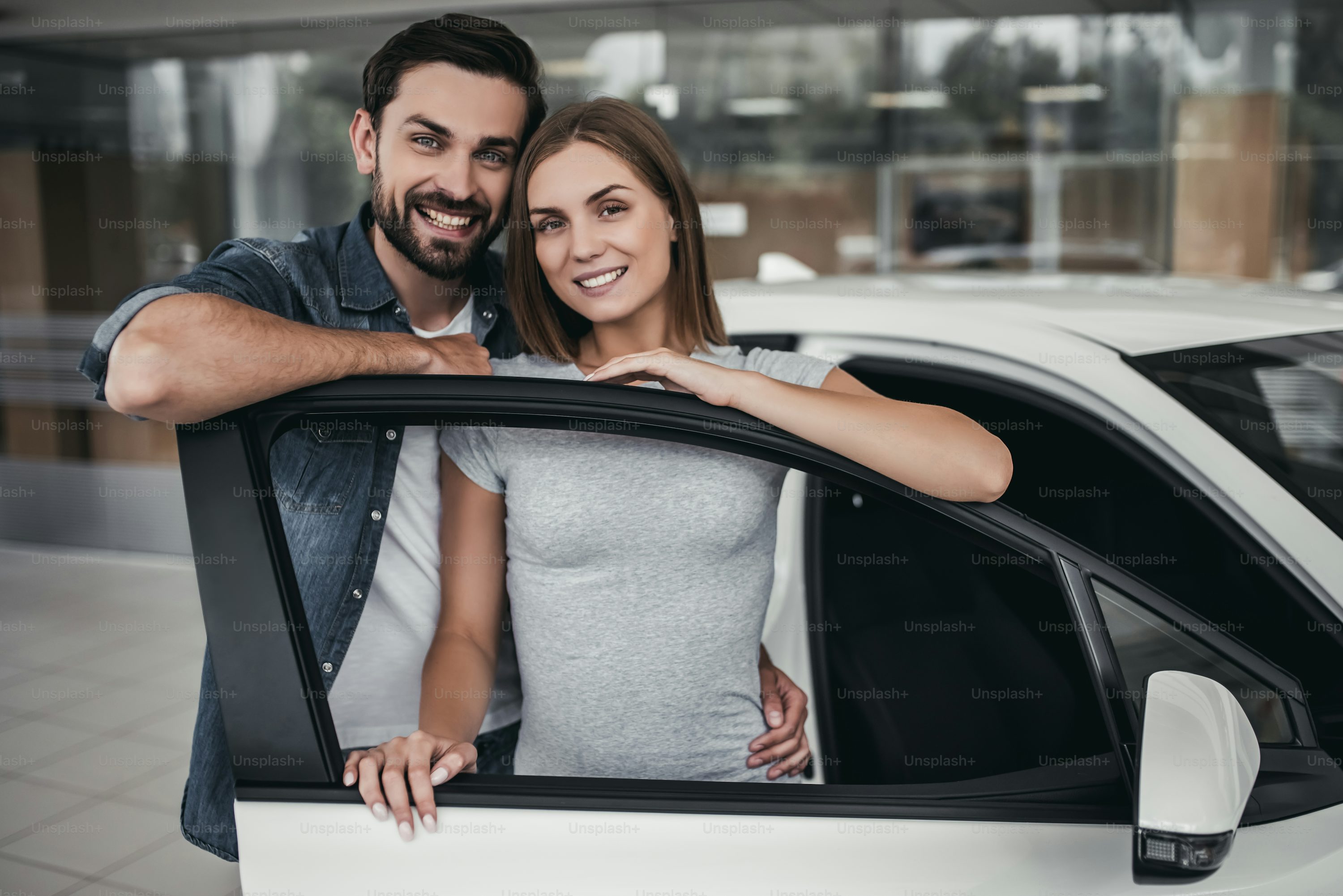 Happy beautiful couple is choosing a new car at dealership, smiling and looking at camera.