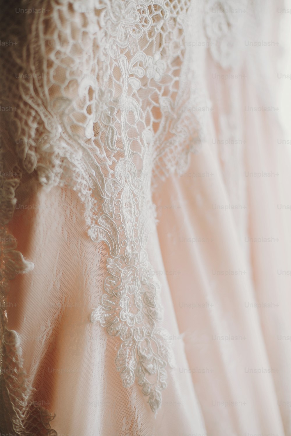 Robe de mariée moderne de luxe suspendue à la fenêtre. Incroyable robe de mariée élégante avec des détails floraux en dentelle, couleur rose pastel. Salon de mariage