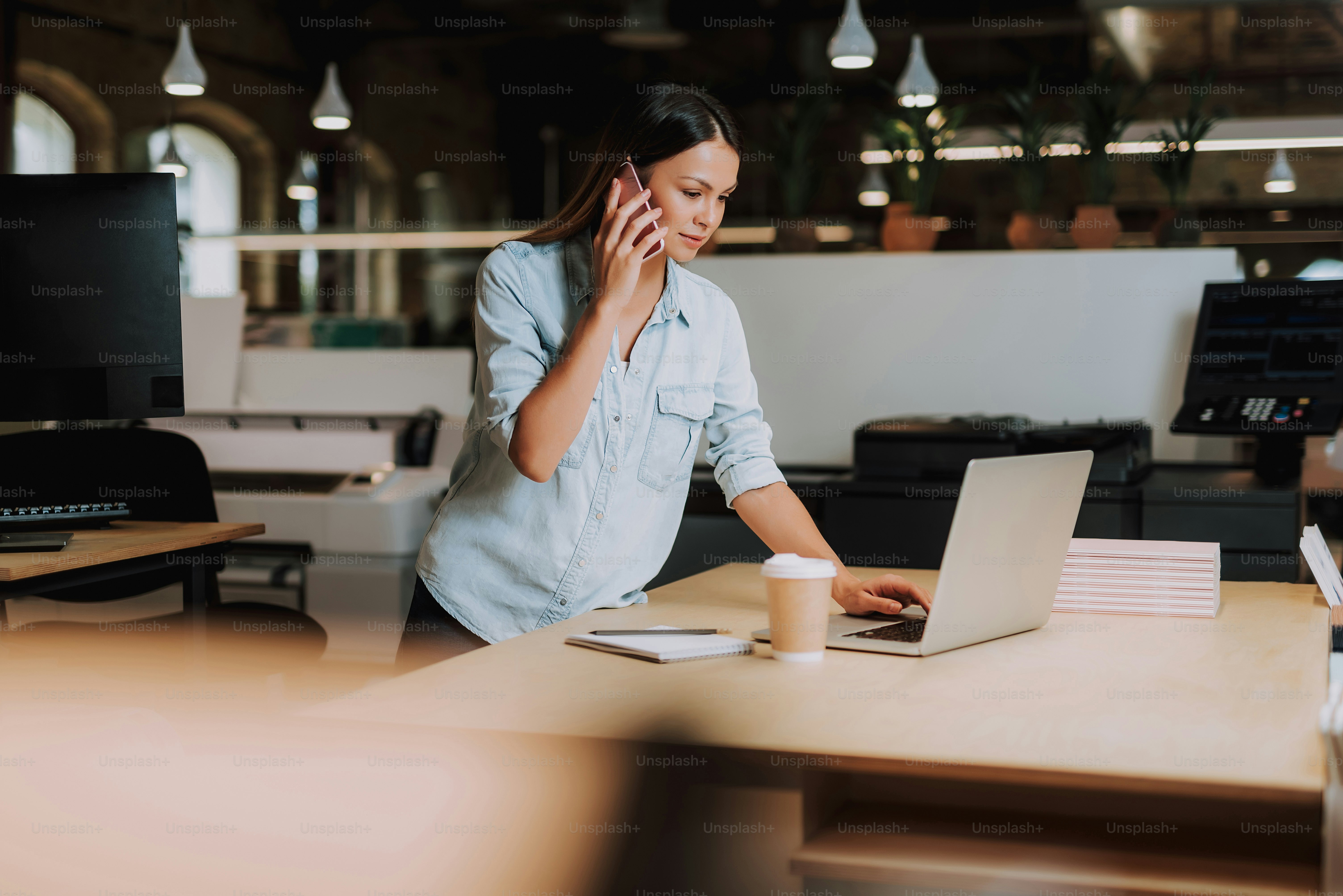 Business call. Waist up portrait of charming woman having phone conversation while standing near office desk and using notebook