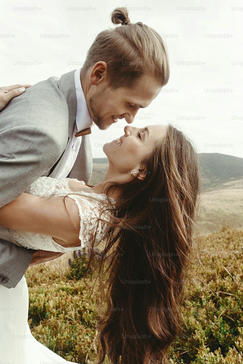 stylish groom happy holding happy bride in sun light and smiling, romantic moment, boho wedding couple, luxury ceremony at mountains with amazing view