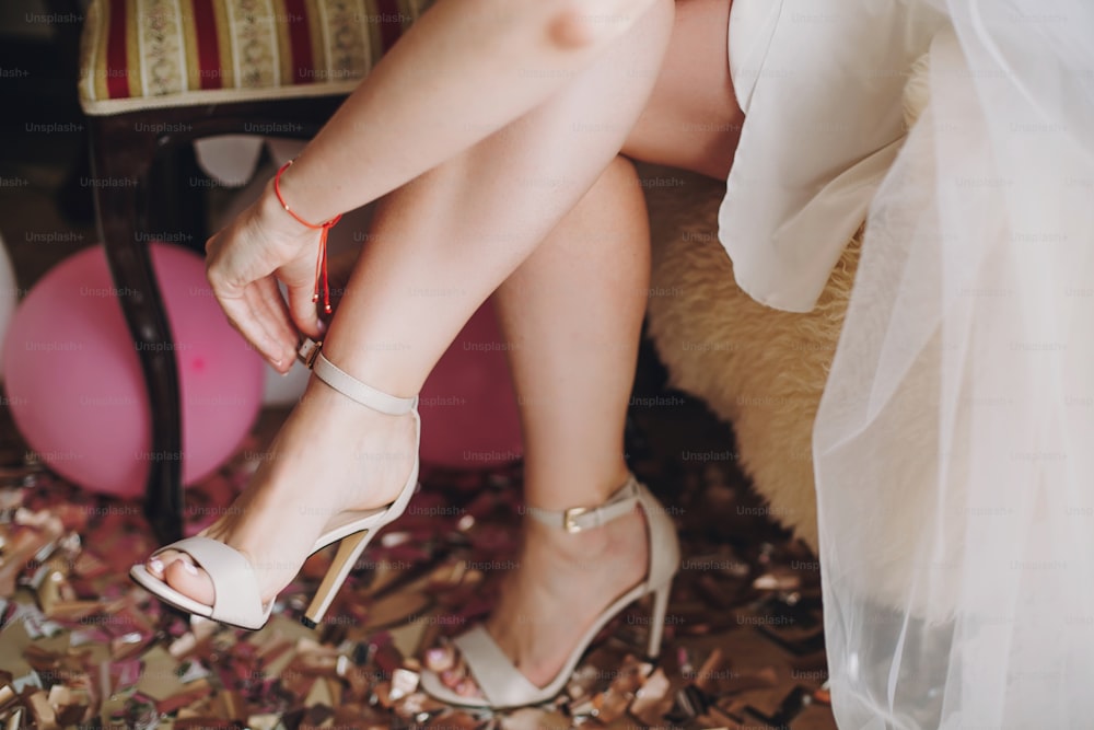 Fille mettant des chaussures blanches élégantes sur des confettis d’or et d’argent, détails du matin de boudoir de mariée avant la cérémonie de mariage. Douche de poule. Fêtes de Noël et du Nouvel An. Parti