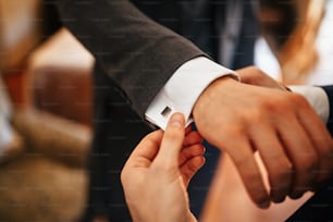 Close up of man helping groom to in getting dressed and adjusting sleeves on his suit before the ceremony.