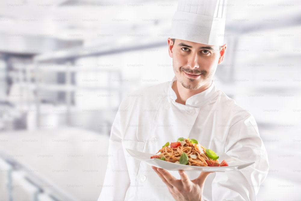 Chef in restaurant kitchen holding plate with italian meal spaghetti bolognese.