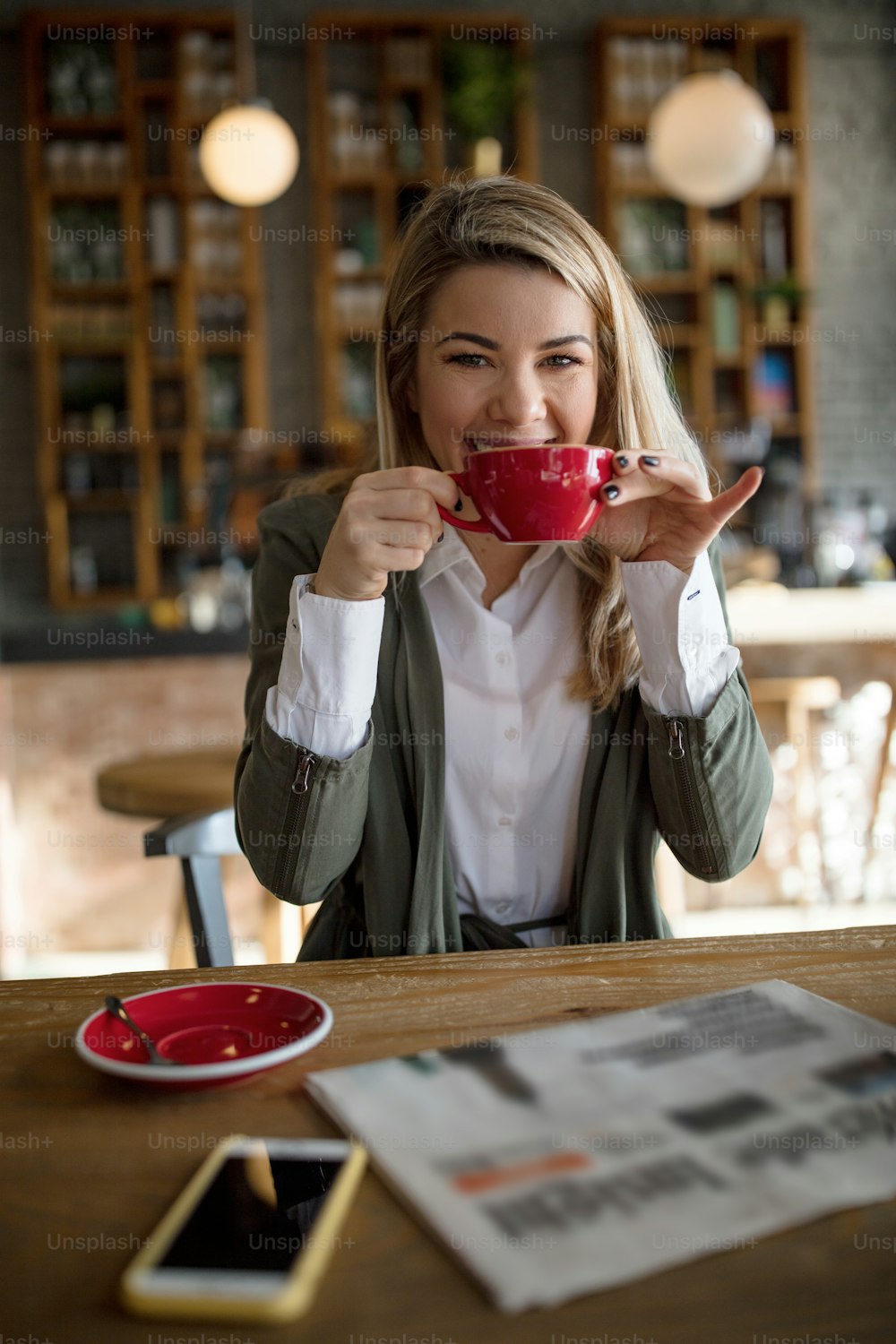 Junge glückliche Geschäftsfrau, die eine Tasse Kaffee genießt, während sie sich im Café entspannt.