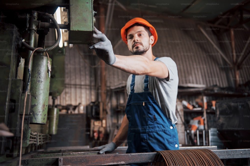 Porträt eines jungen Arbeiters mit Schutzhelm in einer großen Müllrecyclingfabrik. Der Ingenieur überwacht die Arbeit von Maschinen und anderen Geräten.