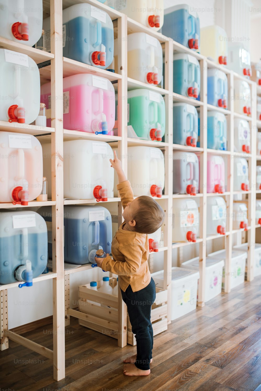 A cute small toddler boy standing by dispensers in zero waste shop.
