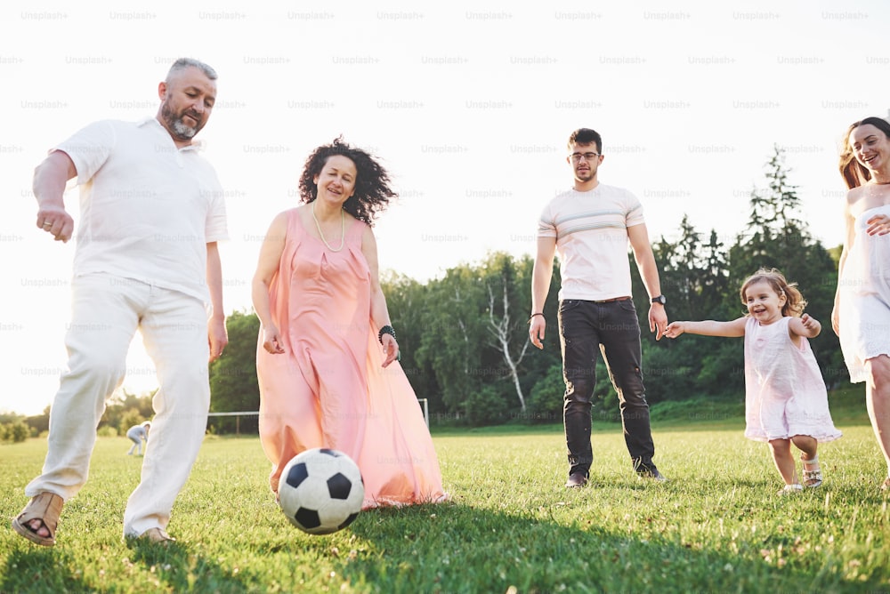 온 가족이 함께 휴식을 취하십시오. 여러 성별 세대가 공원에서 산책을 위해 모였습니다. 손녀와 할아버지는 축구를합니다.