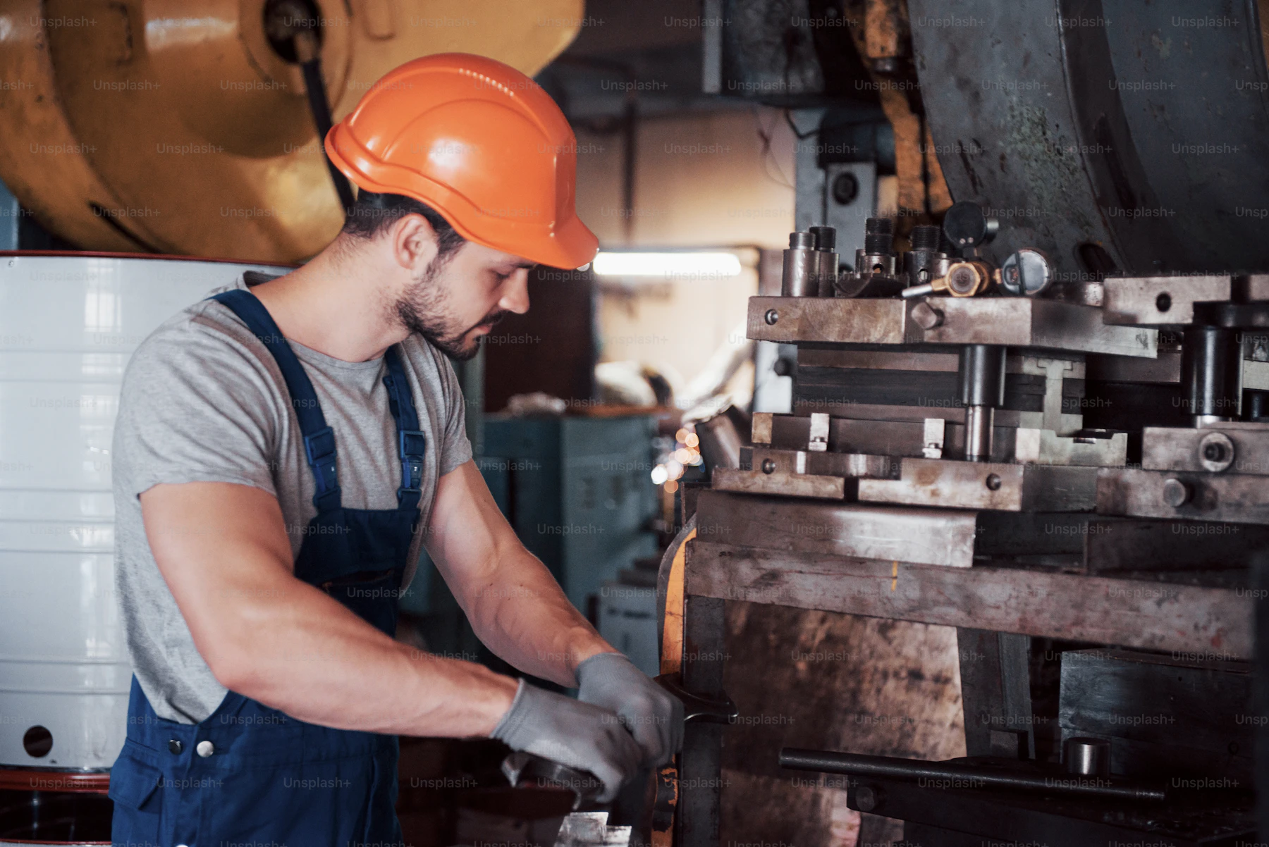 Technician in hard hat and safety vest working hands-on with a machine