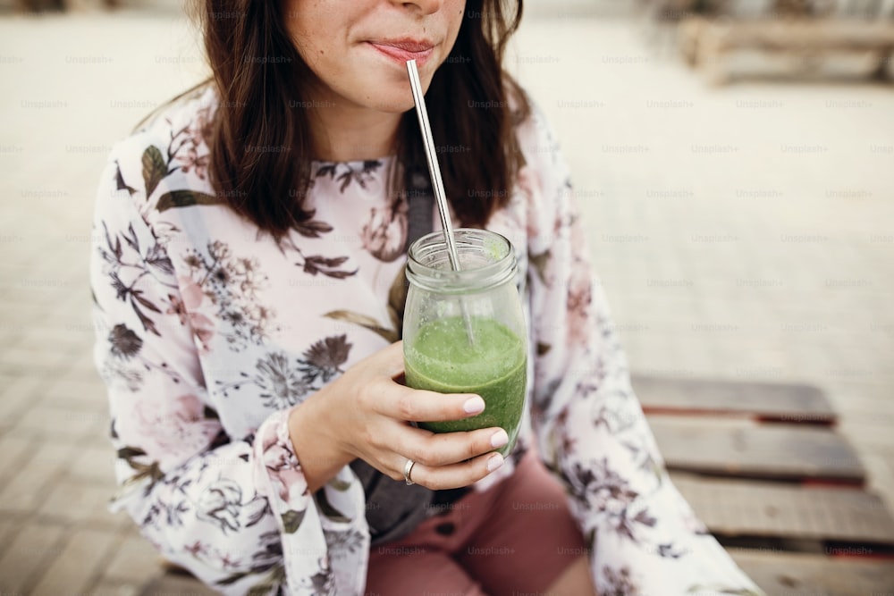 Residuo cero en el festival de comida callejera. Elegante chica boho hipster bebiendo batido de espinacas en frasco de vidrio con pajita reutilizable de metal en el festival de comida callejera. Mujer feliz con gafas de sol con bebida saludable