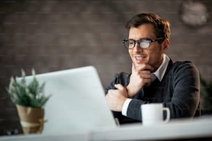 Happy businessman holding hand on chin while working on a computer in the office.