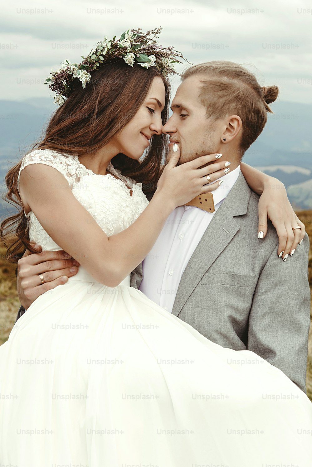 stylish groom  carrying happy bride and hugging, romantic tender moment, boho wedding couple, luxury ceremony at mountains