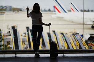 Silhueta da mulher nova no aeroporto internacional, olhando através da janela para os aviões