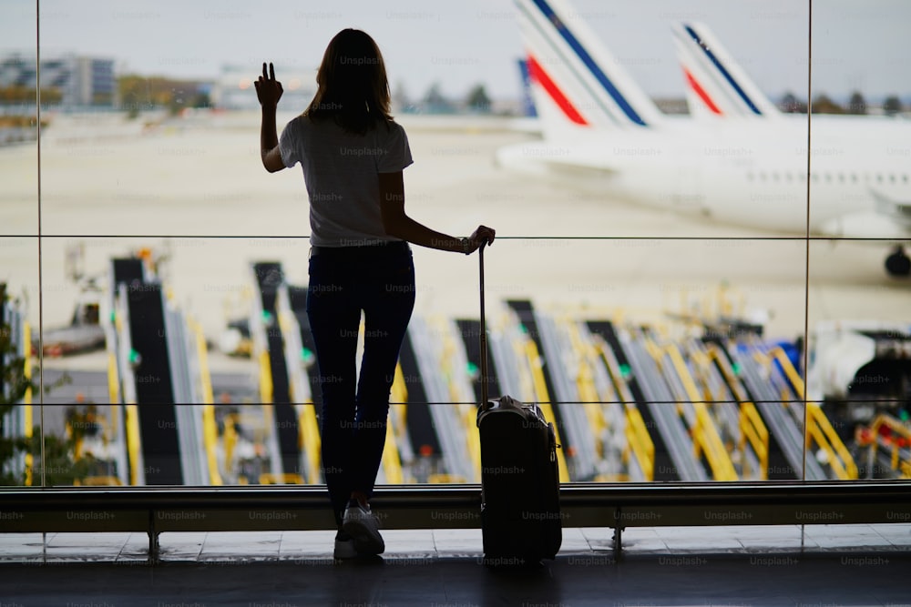 Silueta de mujer joven en el aeropuerto internacional, mirando a través de la ventana a los aviones