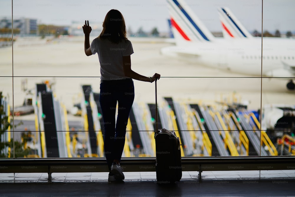 Silhouette of young woman in international airport, looking through the window at planes