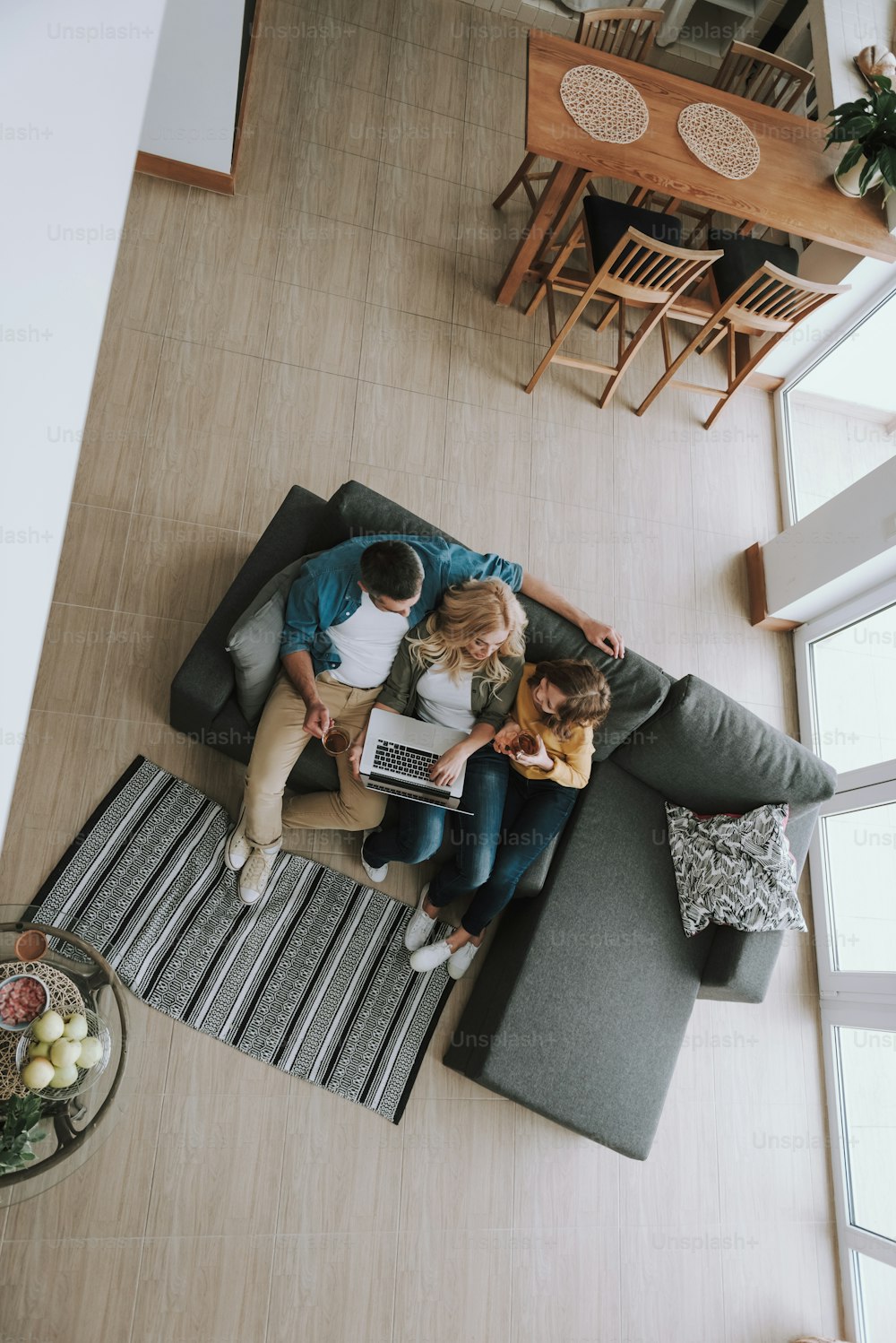 Top view portrait of family sitting on couch and watching videos on laptop. They drinking tea and chatting