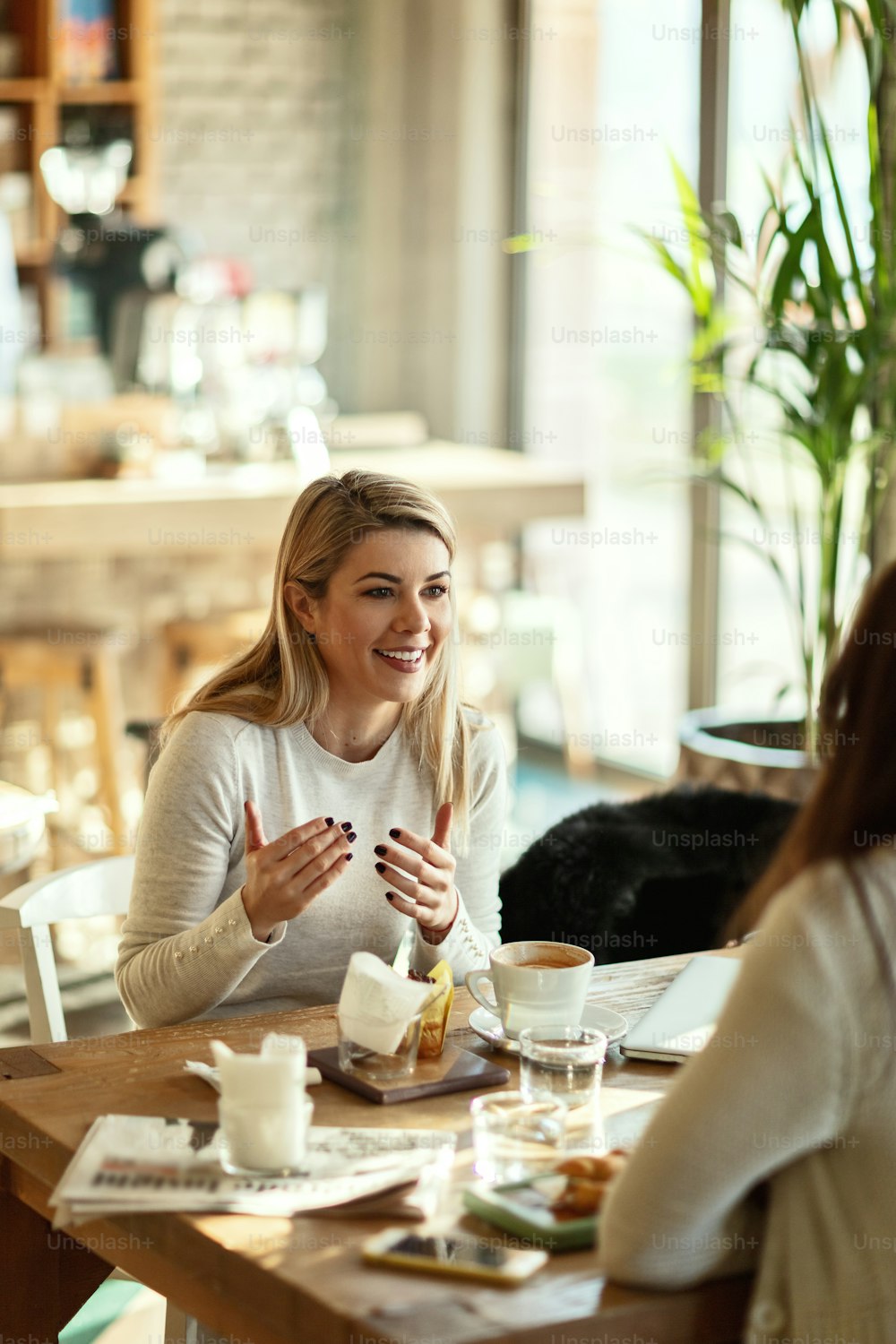 Glückliche Frau, die im Café genießt, während sie mit ihrer Freundin spricht.