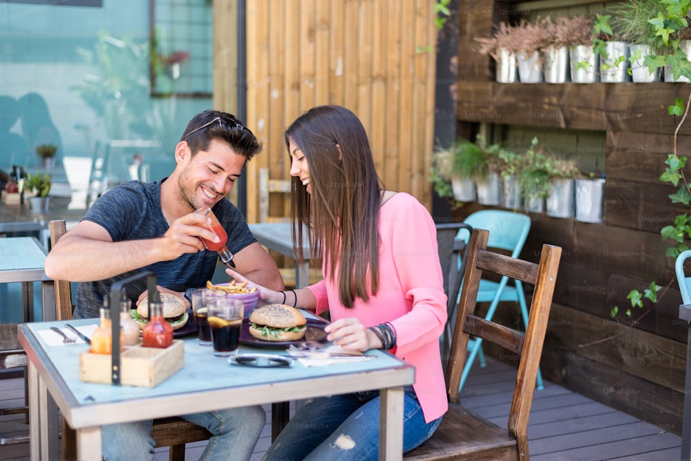 Happy young couple seating in a restaurant terrace eating a burger