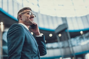 Low angle top view photo of cheerful trendy man speaking on cellular phone and smiling nice against blurred background