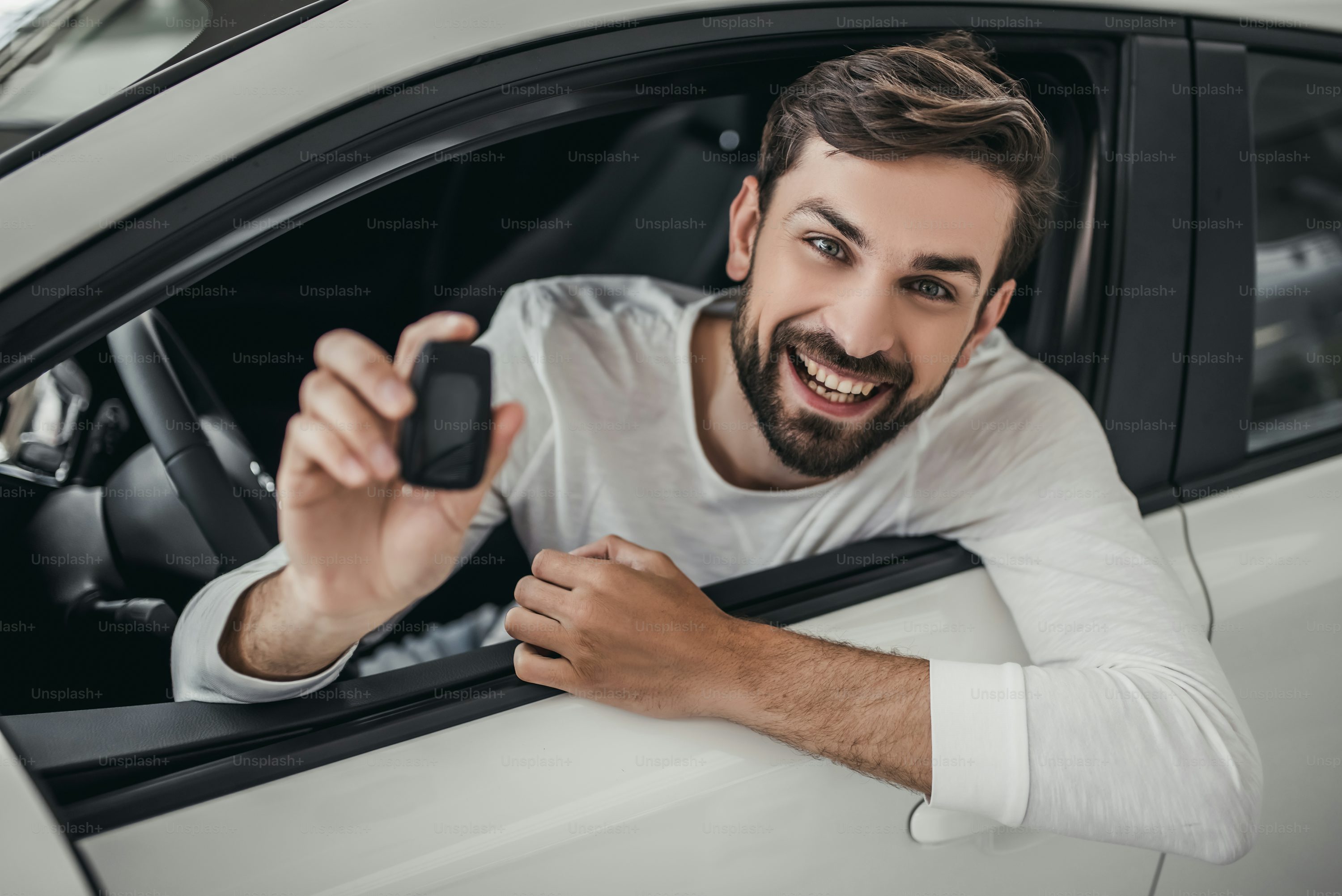 Young man is choosing a new vehicle in car dealership. Holding keys in hand, smiling and looking at the camera.