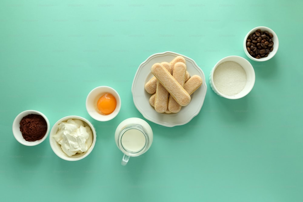 Ingredientes para cocinar tiramisú: galletas bizcochos (Savoiardi, Ladyfinger, galleta), mascarpone, nata, azúcar, cacao, café y huevo sobre fondo azul. Vista superior. Tendido plano