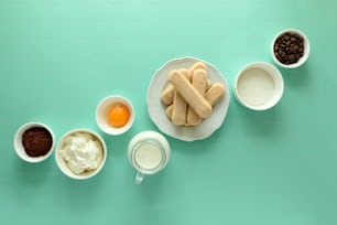 Ingredients for cooking tiramisu: sponge fingers cookies (Savoiardi, Ladyfinger, biscuit), mascarpone, cream, sugar, cocoa, coffee and egg on blue background. Top view. Flat lay