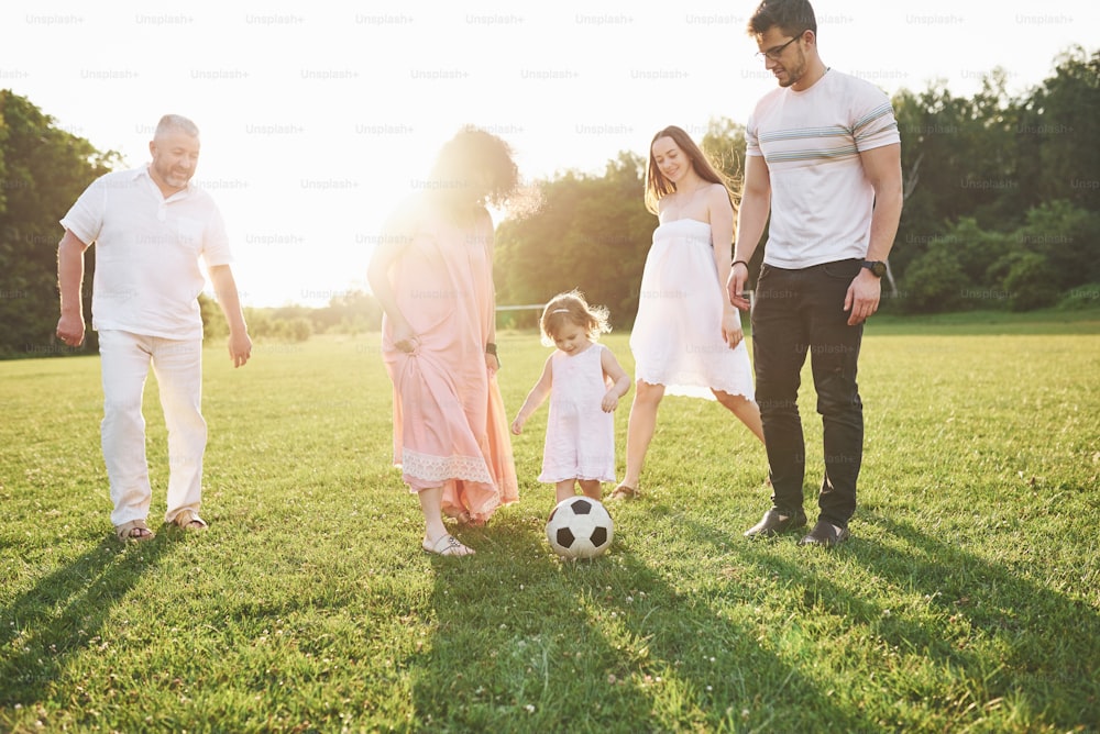 Entspannen Sie mit der ganzen Familie. Mehrere Geschlechtergenerationen kamen zu einem Spaziergang im Park zusammen. Enkelin und Großvater spielen Fußball.