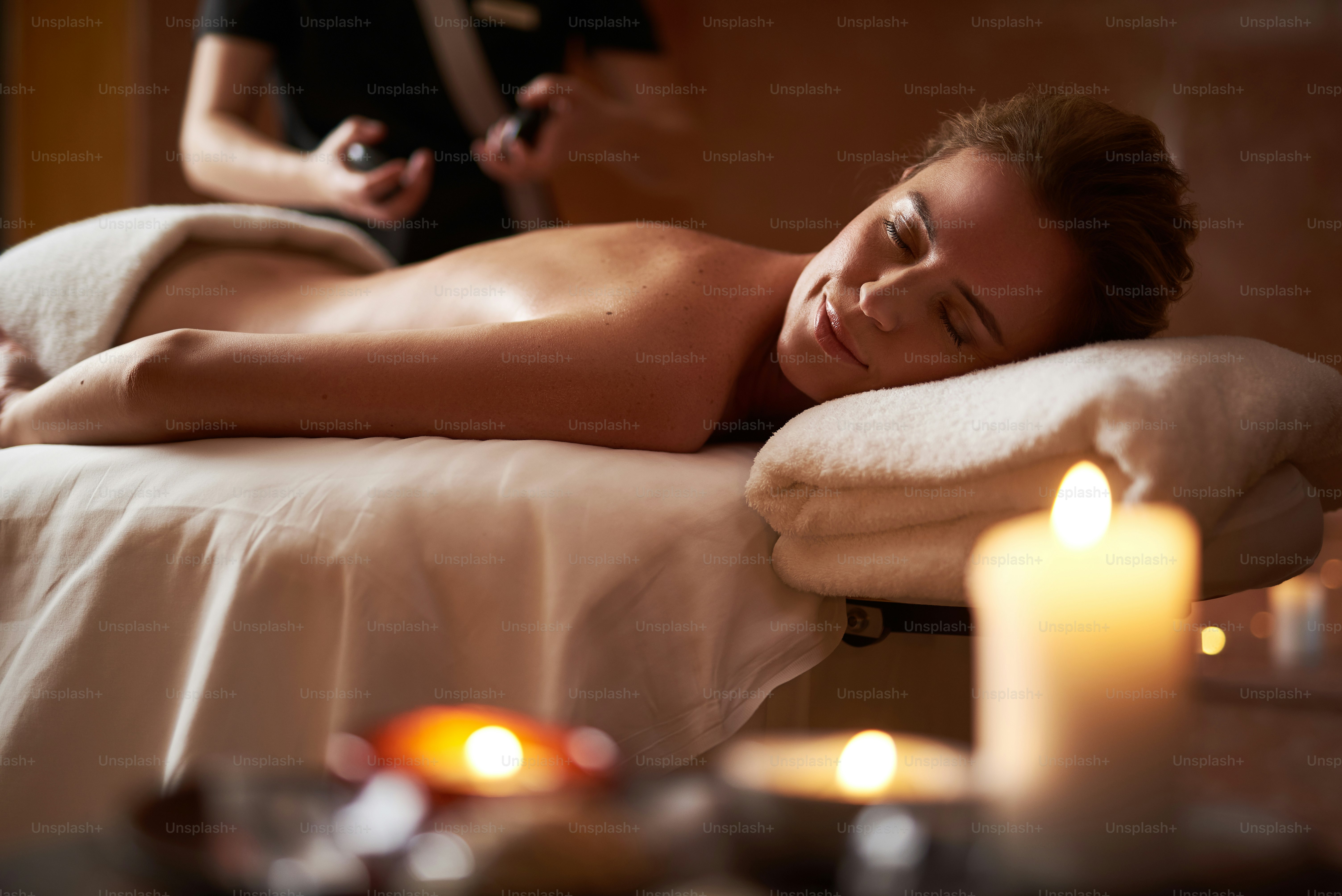 Konsep relaksasi dan perawatan tubuh. Potret wanita muda tersenyum melakukan pijat anti-usia yang santai dengan batu hangat di salon kecantikan dan spa