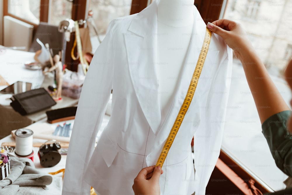 The main thing is right size. Woman designer is measuring white shirt with tape, close-up