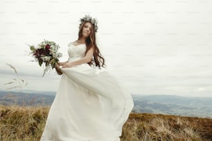 magnifique mariée dansant et s’amusant à tenir une robe, mariage bohème, cérémonie de luxe à des montagnes